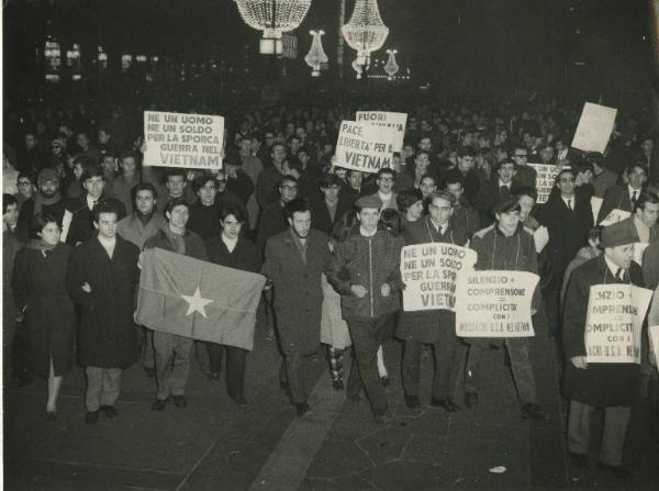 Milano - Manifestazione per il Vietnam - Corteo notturno di giovani recanti cartelli - Luminarie - Bandiere