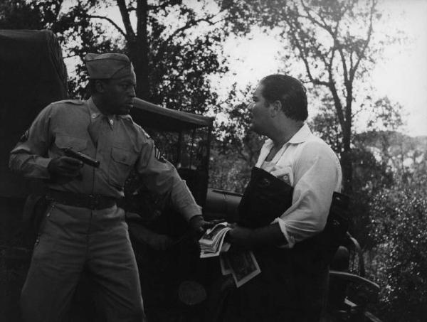 Scena del film "Senza pietà" - Regia Alberto Lattuada - 1948 - Gli attori John Kitzmiller, in divisa militare con una pistola, e Folco Lulli con dei soldi in mano