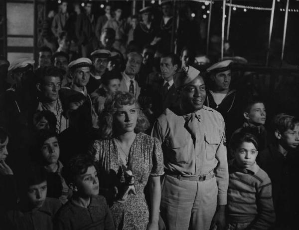 Scena del film "Senza pietà" - Regia Alberto Lattuada - 1948 - Gli attori John Kitzmiller e Carla Del Poggio attorno a un gruppo di attori non identificati