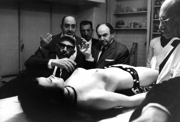 Set del film "Don Giovanni in Sicilia" - Regia Alberto Lattuada - 1967 - Il regista Alberto Lattuada e gli operatori della troupe osservano il manichino di una donna nuda stesa sul tavolo