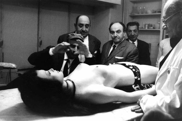 Set del film "Don Giovanni in Sicilia" - Regia Alberto Lattuada - 1967 - Il regista Alberto Lattuada e gli operatori della troupe osservano il manichino di una donna nuda stesa sul tavolo