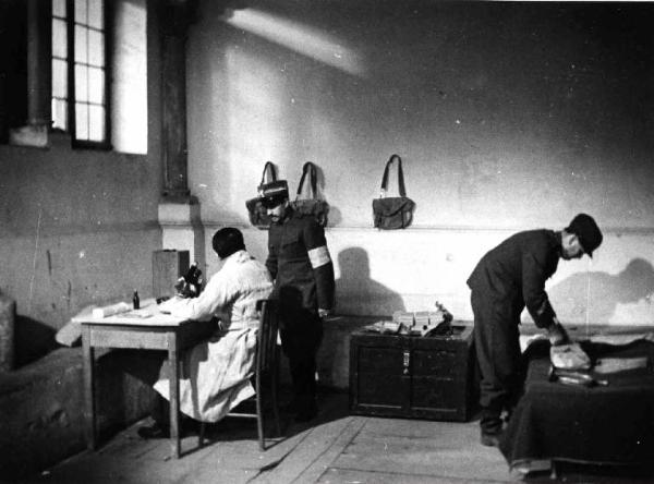 Set del film documentario "Anopheles" - Regia Giampiero Pucci - 1950 - Un uomo in camice bianco seduto a una scrivania e due in divisa militare