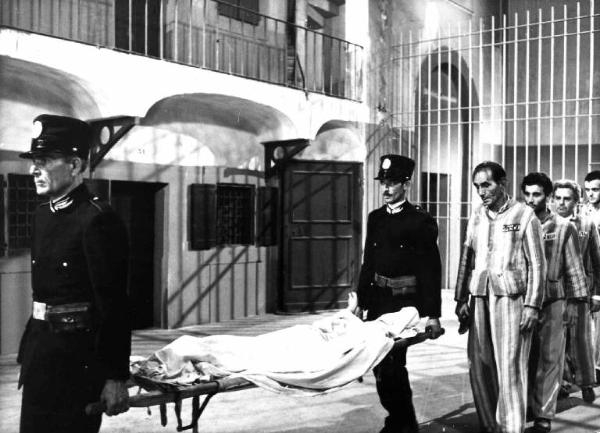 Scena del film "Antonio Gramsci: i giorni del carcere" - Regia Lino Del Fra - 1977 - Una fila di carcerati segue due uomini indivisano che trasportano un corpo coperto in barella