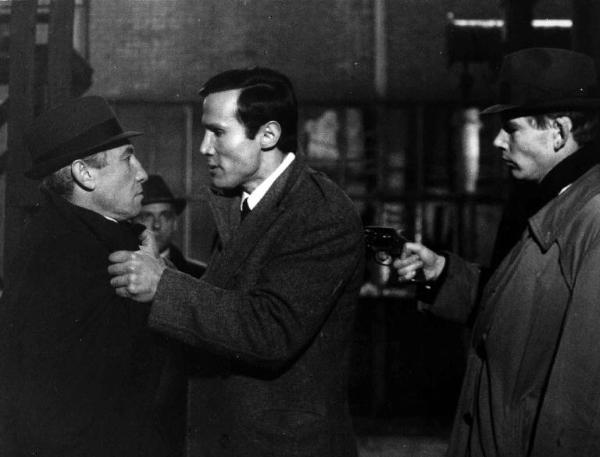Scena del film "Assassination" - Regia Emilio Miraglia - 1967 - Un attore non identificato punta la pistola contro la schiena di Henry Silva