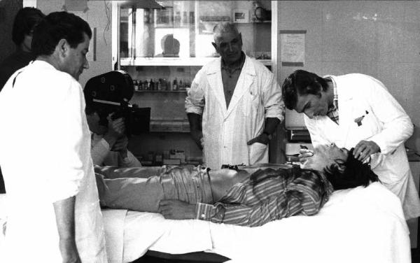 Scena del film "La Circostanza" - Regia Ermanno Olmi- 1974 - Attore non identificato con camice bianco visita un attore non identificato sul lettino, attorno altri attori non identificati con camice bianco.