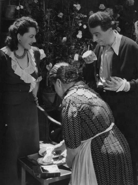 Scena del film "Confessione" - Regia Flavio Calzavara - 1941 - L'attrice Paola Barbara sorride all'attore Aldo Silvani, mentre un'attrice non identificata sistema un tavolino