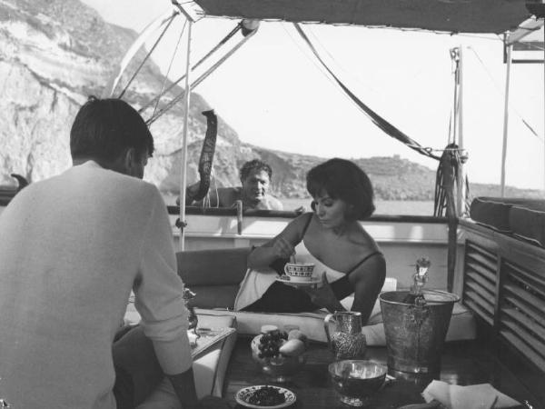 Set del film "La Corruzione" - Regia Mauro Bolognini- 1964- L'attore Jacques Perrin di spalle, l'attrice Rosanna Schiaffino seduti in una barca e l'attore Alain Cuny che risale sulla stessa barca.