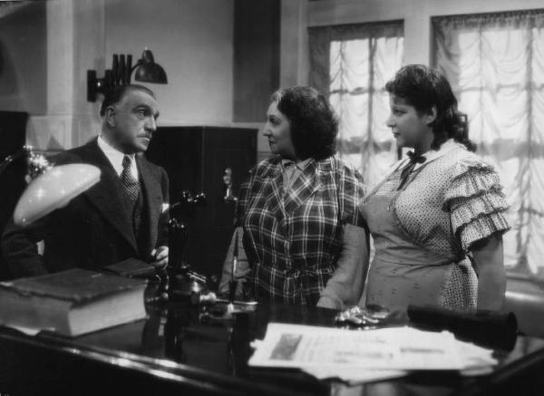 Set del film "Cose dell'altro mondo" - Regia Nunzio Malasomma - 1939- L'attore Antonio Gandusio, l'attrice Amelia Chellini e l'attrice Wanda Gloria dietro un tavolo in un interno.