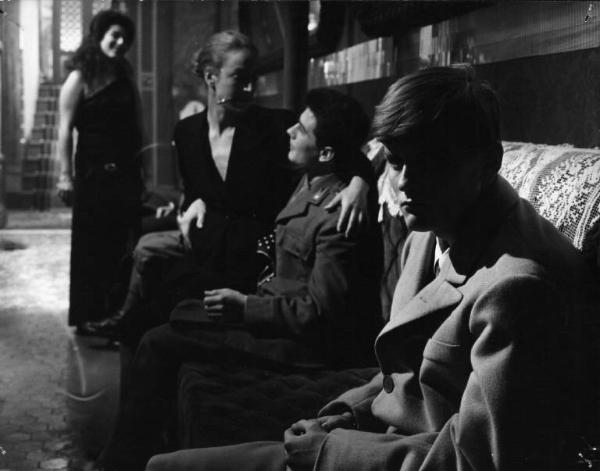Set del film "Cronaca familiare" - Regia Valerio Zurlini 1962 - L'attore Jacques Perrin seduto su un divano con altre persone nella penombra.