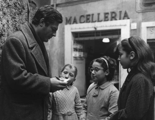 Set del film "Cronaca familiare" - Regia Valerio Zurlini 1962 - L'attore Marcello Mastroianni con delle bambine davanti ad una macelleria.