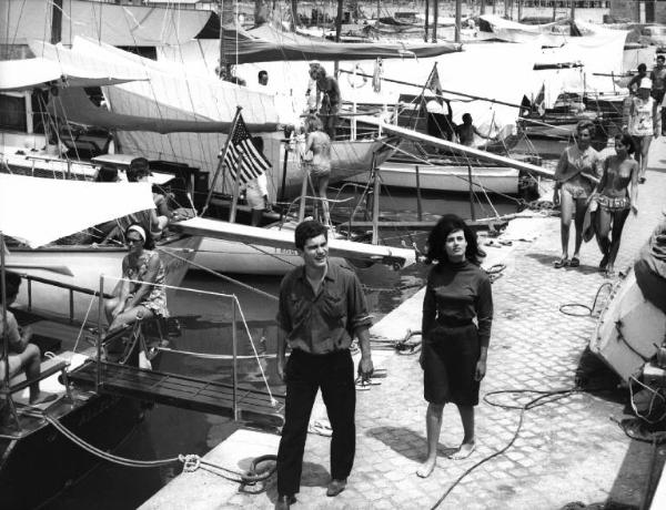 Fotografia del film "La cuccagna" - Regia Luciano Salce 1962 - L'attore Luigi Tenco e l'attrice Donatella Turri camminano su un molo.
.