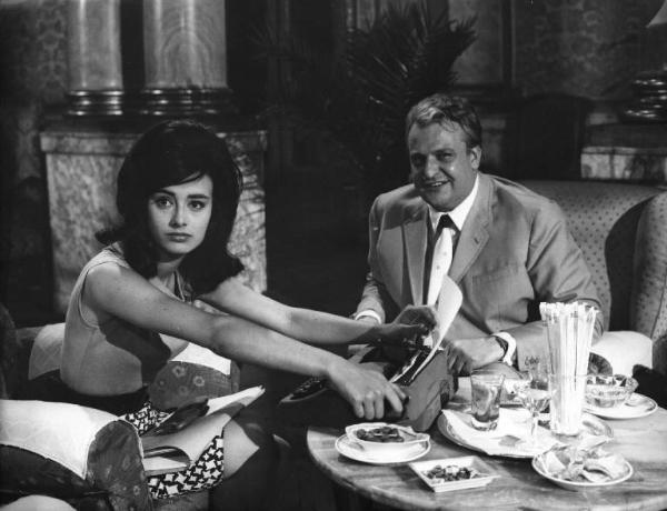 Fotografia del film "La cuccagna" - Regia Luciano Salce 1962 - L'attrice Donatella Turri estrae un foglio da una macchina da scrivere seduta ad una tavolino da aperitivo con l'attore Umberto D'Orsi.
