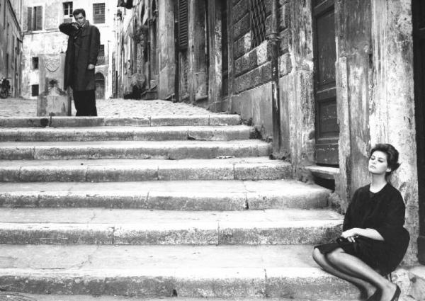 Fotografia del film "I delfini" - Regia Francesco Maselli 1960 - L'attrice Claudia Cardinale seduta su uno scalino e l'attore Sergio Fantoni vicino a una fontana.