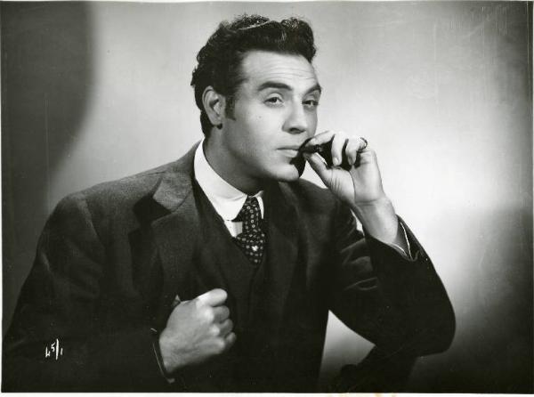 Scena del film "Il delitto di Giovanni Episcopo" - Regia Alberto Lattuada, 1947 - Mezza figura di Roldano Lupi. Tiene un sigaro in bocca con la mano sinistra e il bavero della giacca con la destra.