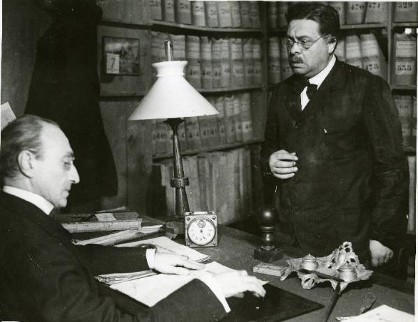 Scena del film "Il delitto di Giovanni Episcopo" - Regia Alberto Lattuada, 1947 - Gino Cavalieri è seduto alla sua scrivania e guarda delle carte. Di fronte a lui, in piedi, Aldo Fabrizi.