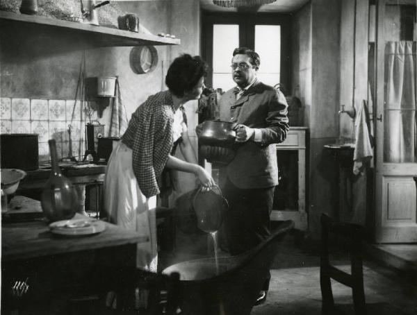 Scena del film "Il delitto di Giovanni Episcopo" - Regia Alberto Lattuada, 1947 - Yvonne Sanson chinata mentre rovescia un secchio di acqua calda in un grande catino. Aldo Fabrizi, in piedi di fronte a lei, tiene in mano una brocca.