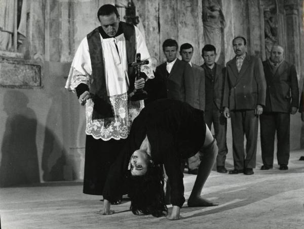 Scena del film "Il demonio" - Regia Brunello Rondi, 1963 - In una chiesa, Giovanni Cristofanelli esorcizza Daliah Lavi con acqua santa e crocifisso. L'attrice ha il corpo in posizione a ponte. Sullo sfondo, un gruppetto di uomini.