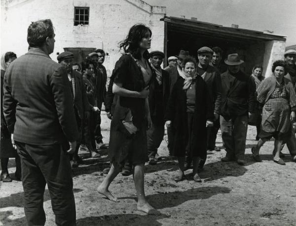 Scena del film "Il demonio" - Regia Brunello Rondi, 1963 - Daliah Lavi cammina tra la gente del paese, che la guarda indignata. L'attrice scalza e con i vestiti laceri, avanza con espressione smarrita tenendosi una mano sulla pancia.