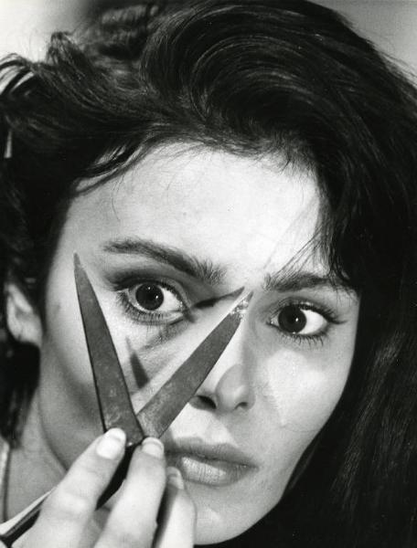Scena del film "Il demonio" - Regia Brunello Rondi, 1963 - Primo piano di Daliah Lavi. Con la mano destra tiene un paio di forbici, vicine al viso, con le lame semiaperte incorniciando in una "V" l'occhio destro.