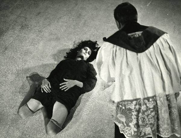 Scena del film "Il demonio" - Regia Brunello Rondi, 1963 - Daliah Lavi è stesa supina a terra con le gambe piegate sotto i glutei e le mani sul ventre. Giovanni Cristofanelli, in piedi, di spalle, le mostra il crocifisso.