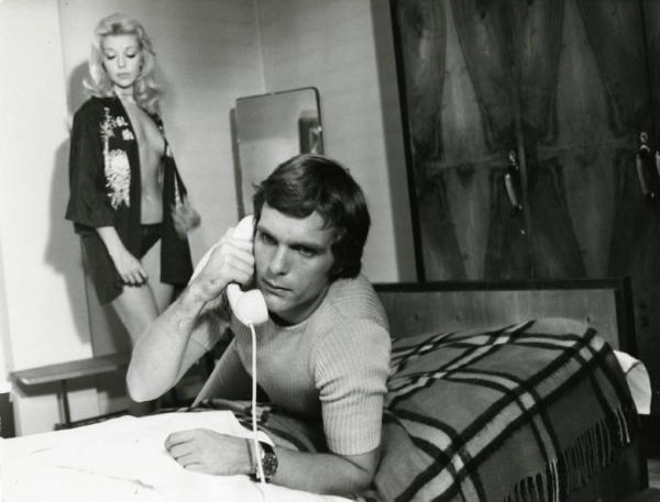 Scena del film "Il diavolo nel cervello" - Regia Sergio Sollima, 1972 - Keir Dullea, semisdraiato sul letto risponde al telefono. Sullo sfondo, in piedi, Gabriella Lepori, con indosso mutande e giacca di un kimono.