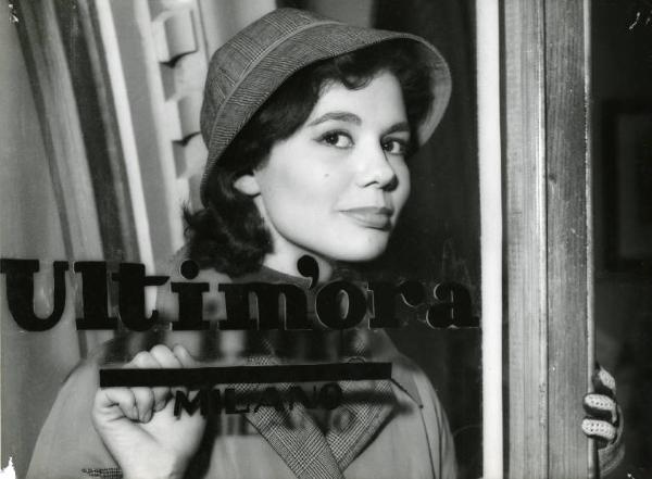 Scena del film "Difendo il mio amore" - Regia Giulio Macchi, 1956 - Mezza figura di Giorgia Moll in piedi dietro a una porta a vetri con la scritta Ultim'ora Milano.