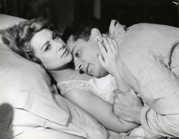 Scena del film "Difendo il mio amore" - Regia Giulio Macchi, 1956 - Martine Carol sdraiata supina a letto, ha la mano destra sul viso di Gabriele Ferzetti che è sdraiato sopra di lei, con la testa appoggiata al petto.