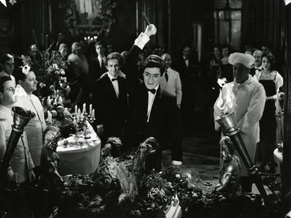 Scena del film "Il disordine" - Regia Franco Brusati, 1962 - Sami Frey, in smoking, durante una festa, alza un pugnale sopra la sua testa per infilzare un maiale arrosto con l'attenzione di tutti i presenti.