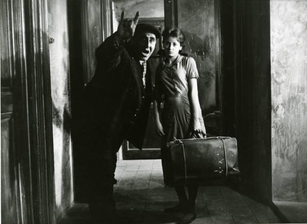 Scena del film "Divorzio all'italiana" - Regia Pietro Germi, 1961 - Figura intera di un uomo e Margherita Girelli in piedi davanti a una porta. Lui fa il gesto delle corna mentre lei regge una valigia.