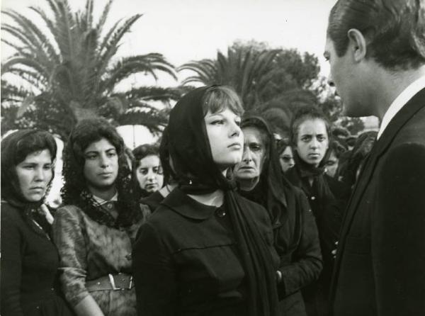 Scena del film "Divorzio all'italiana" - Regia Pietro Germi, 1961 - Stefania Sandrelli, vestita a lutto, guarda negli occhi Marcello Mastroianni. Alle sue spalle, un gruppo di donne li osserva.