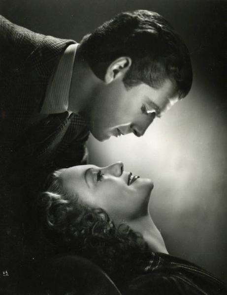 Scena del film "Documento Z 3" - Regia Alfredo Guarini, 1942 - Primo piano di profilo di Claudio Gora e Isa Miranda. L'attrice appoggia la testa su uno schienale e solleva il mento. Alle sue spalle, l'attore, avvicina il viso a quello di lei.