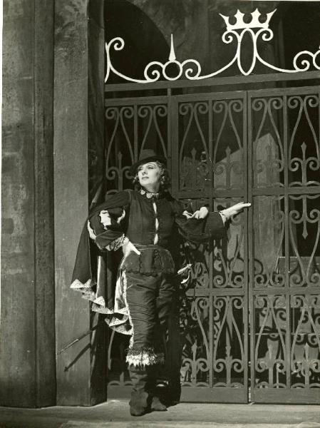 Sul palco dello spettacolo teatrale "La dodicesima notte" - Regia Renato Castellani, 1957 - Figura intera di Rina Morelli, in abiti di scena, appoggiata a un cancello.