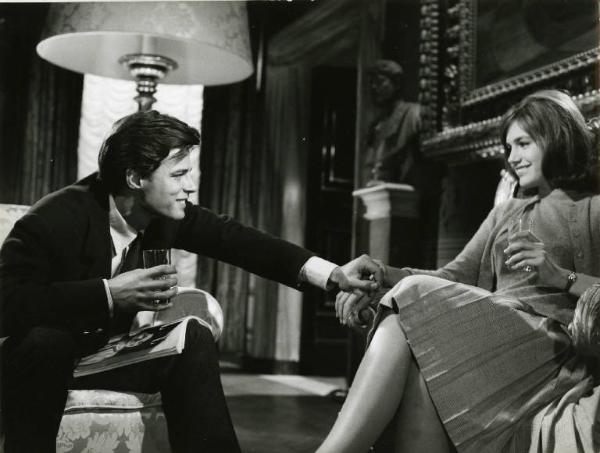 Scena del film "I dolci inganni" - Regia Alberto Lattuada, 1960 - Piano americano di Jean Sorel, seduto, che si sporge verso Catherine Spaak, seduta di fronte a lui, per stringerle la mano. I due, si guardano, sorridono e hanno un bicchiere in mano.