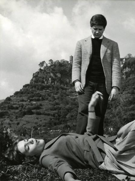Scena del film "I dolci inganni" - Regia Alberto Lattuada, 1960 - Catherine Spaak è sdraiata supina sull'erba, di profilo, con gli occhi chiusi e un braccio alzato. Al suo fianco, in piedi, in figura intera, Oliviero Prunas, guarda per terra.