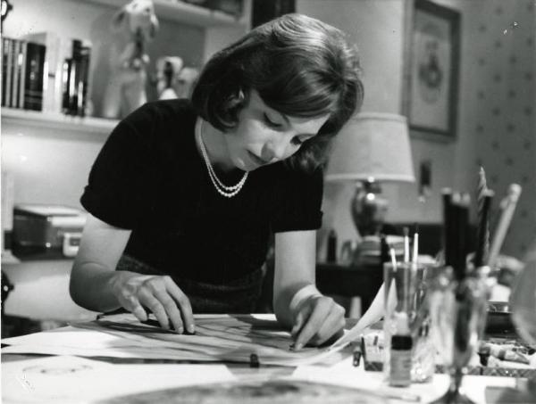 Scena del film "I dolci inganni" - Regia Alberto Lattuada, 1960 - Mezza figura di un'attrice non identificata seduta a una scrivania, con la testa china, disegna su un foglio.