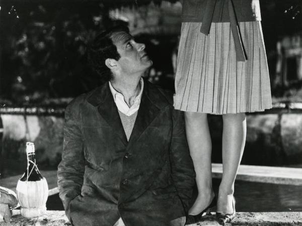 Scena del film "I dolci inganni" - Regia Alberto Lattuada, 1960 - Mezza figura di Christian Marquand appoggiato al bordo di una fontana. Accanto a lui, in piedi sul bordo, una ragazza inquadrata dalla vita in giù.
