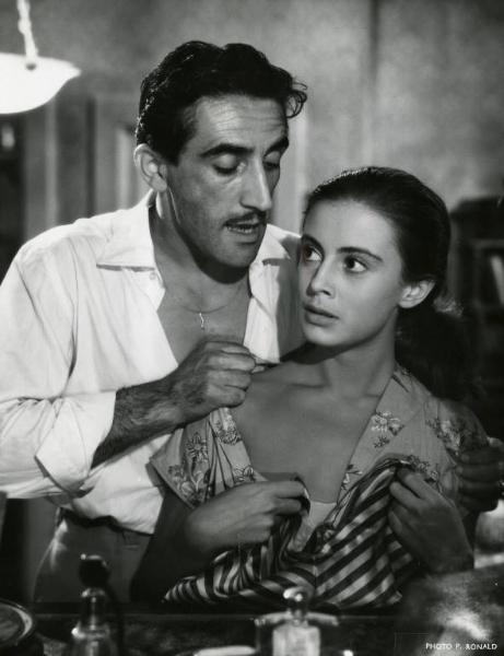 Scena del film "Domani è un altro giorno" - Regia Léonide Moguy, 1951 - Mezza figura di Arnoldo Foà, in piedi dietro ad Anna Maria Ferrero. L'attore le abbassa il vestito, scoprendole una spalla.