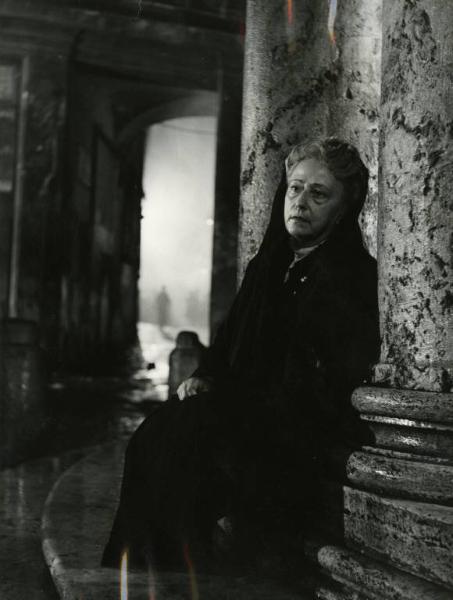 Scena del film "Domani è un altro giorno" - Regia Léonide Moguy, 1951 - Figura intera di Rina De Liguoro, vestita a lutto, seduta su uno scalino tra due colonne.