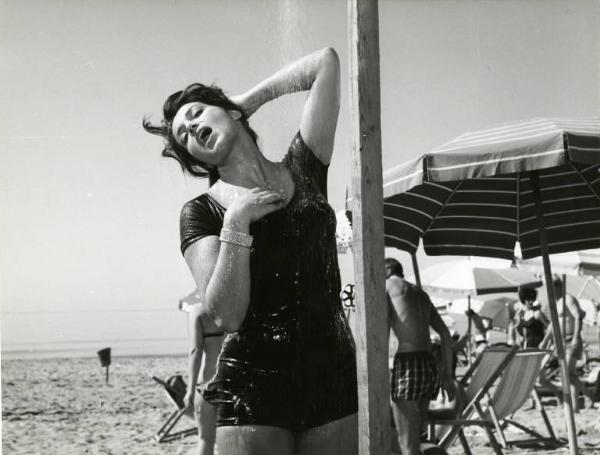 Scena del film "Una domenica d'estate" - Regia Giulio Petroni, 1962 - Piano americano di Françoise Fabian, in costume, mentre si fa la doccia. Sullo sfondo, il mare. A destra sdraio, ombrelloni, bagnanti.