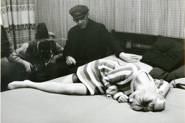 Sul set del film "Don Giovanni in Sicilia" - Regia Alberto Lattuada, 1967 - Ewa Aulin, sdraiata su un fianco, di traverso al letto. Sullo sfondo, Alberto Lattuada seduto dietro la macchina da presa e un altro membro della troupe.