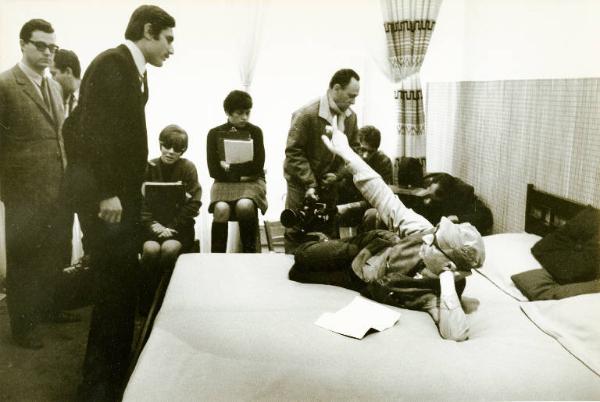Sul set del film "Don Giovanni in Sicilia" - Regia Alberto Lattuada, 1967 - Totale. Alberto Lattuada disteso a letto sul fianco, alza un braccio e l'indice verso l'alto, mentre con l'altro si regge la testa. Lando Buzzanca è in piedi di fronte a lui.