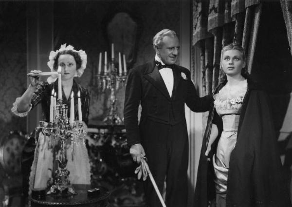 Scena del film "La donna perduta" - Regia Domenico Gambino, 1940 - Piano americano di un'attrice non identificata mentre accende una candela. Accanto a lei Alberto Capozzi tiene una mano sulla spalla di Luisella Beghi, che guarda nel vuoto.