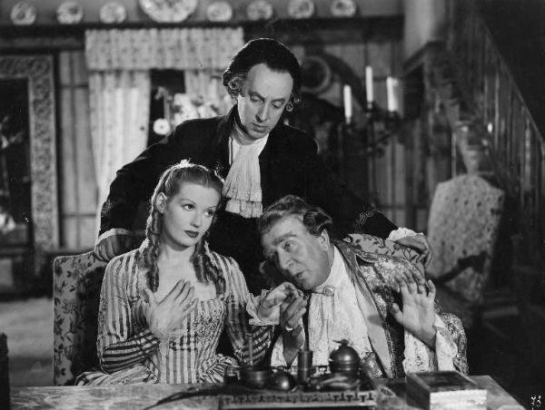 Scena del film "Don Pasquale" - Regia Camillo Mastrocinque, 1940 - Mezza figura di Laura Solari e Armando Falconi che, seduto accanto a lei, finge di baciarle la mano. Alle loro spalle, in piedi, Franco Coop.