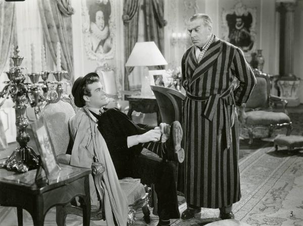 Scena del film "Due cuori sotto sequestro" - Regia Carlo Ludovico Bragaglia, 1941 - Massimo Serato seduto su una poltrona mentre si allaccia una scarpa. A destra, Armando Falconi, in piedi, lo osserva.