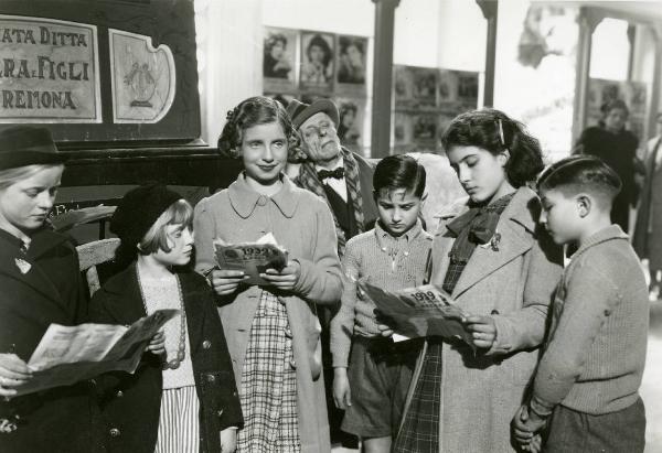 Scena del film "Due milioni per un sorriso" - Regia Carlo Borghesio, Mario Soldati, 1939 - Un gruppo di fanciulli in cerchio con al centro Antonietta Vilella, leggono. In secondo piano Lauro Gazzolo.