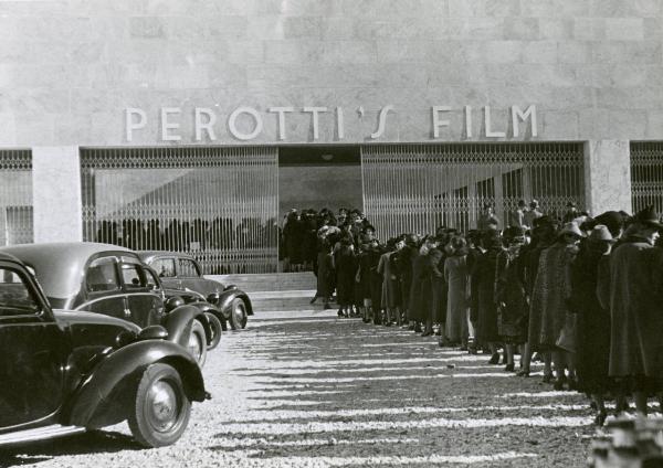 Scena del film "Due milioni per un sorriso" - Regia Carlo Borghesio, Mario Soldati, 1939 - Fila di persone in attesa davanti ai cancelli dello stabilimento cinematografico "PEROTTI'S FILM".