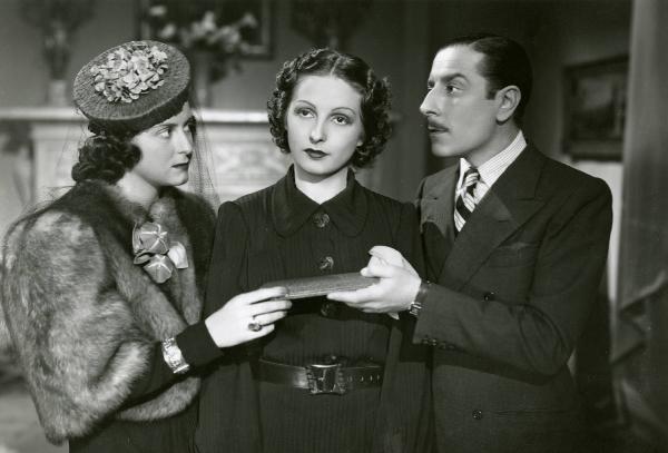 Scena del film "Due occhi per non vedere" - Regia Gennaro Righelli, 1939 - Giuseppe Porelli, sulla destra, tende un oggetto a un'attrice non identificata, sulla sinistra, mentre Loretta Vinci, al centro, guarda davanti a sé.