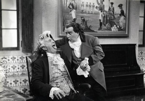 Scena del film "Elisir d'amore" - Regia Amleto Palermi, 1941 - Armando Falconi, in piedi a destra, sorregge la mano destra di Enzo Biliotti, seduto su una poltrona con la lingua fuori dalla bocca e la mano destra sulla fronte.