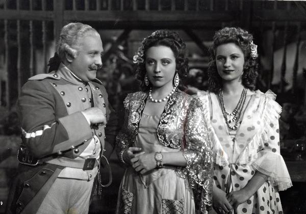 Scena del film "Elisir d'amore" - Regia Amleto Palermi, 1941- A sinistra, un attore non identificato in abiti militari, osserva Margherita Carosio, al centro, e Jone Salinas, a destra.
