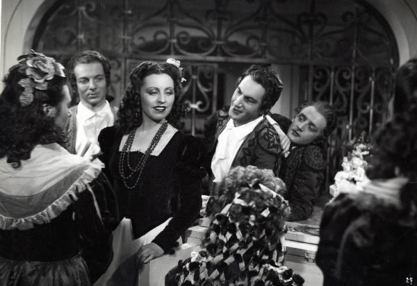 Scena del film "Elisir d'amore" - Regia Amleto Palermi, 1941 - Margherita Carosio, al centro, volge lo sguardo verso il basso, mentre attori non identificati intorno a lei la osservano.